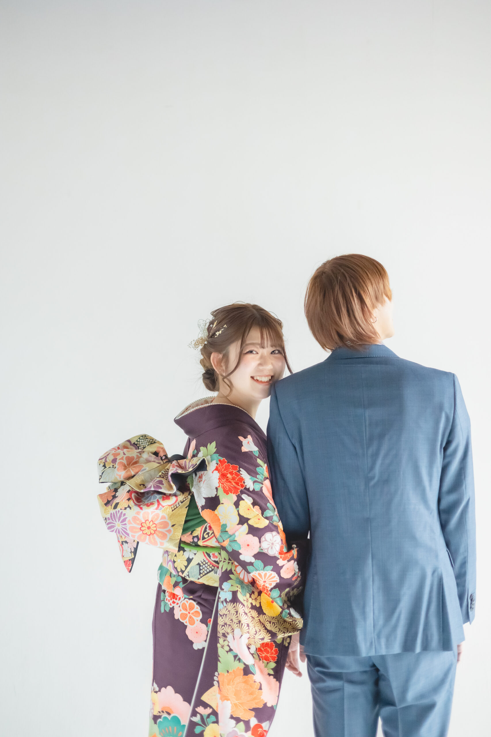 こちらを振り向く振袖の女性とスーツ姿の男性の後姿
